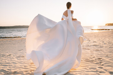 Happy young bride woman in white dress running, have fun on clean sandy beach waves of the sea or ocean on sunset, summer photo shooting near a water. Wedding rest, relax honeymoon concept. - obrazy, fototapety, plakaty