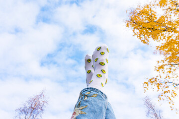 Legs in funny white socks with avocado on the background of clouds and yellow leaves. Autumn sky