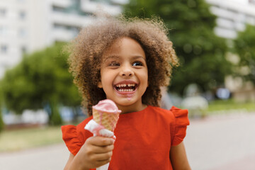 a black laughing child with ice cream in a waffle cone at summer day - Powered by Adobe