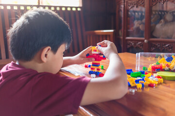 Asian boy is getting creative with assembling colorful plastic bricks into robots and planes on a wooden table happy and fun at home.Kid Creators concept.