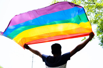 back view shot of young man proudly holding waving lgbtq flag - cocnept of pride month celebration, support and movement. - obrazy, fototapety, plakaty