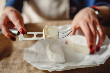 Cut Camembert cheese, French soft cheese with white mold in the hands of a woman on the background...