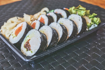 Sliced rolls of salmon and raw tuna sushi in plastic container