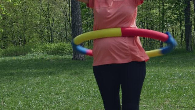 close-up hula hoop exercises on belly outdoor, hula-hoop twirling for weight loss slimming. heavy hooping in park on green grass in sunny daytime. sport outdoors, active lifestyle, health concept