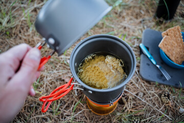 Tourist utensils, camp cooking in a pot, open the lid look inside the pot, cook noodles, a quick meal in nature, lunch in the forest on the grass, trekking in the mountains