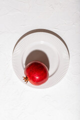 A ripe pomegranate lies on a white plate on a table covered with a white tablecloth, healthy food concept.. Minimalism. Flat lay composition. Top view, copy space.