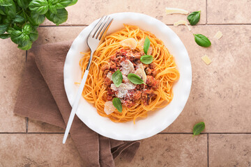 Pasta spaghetti Bolognese. Tasty appetizing italian spaghetti with bolognese sauce, tomato sauce, cheese parmesan and basil on white plate on old beige tiles table background. Top view.