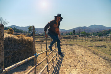 A young man in the image of a cowboy with a hat climb and jumping a fence in front of a haystack....