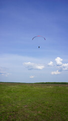 Paraglider flying in blue sky above green field in summer