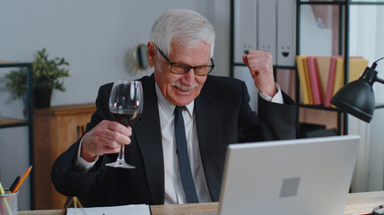 Senior business man freelancer gets good news, positive exam results, opportunity, successfully signed contract, celebrates victory drinking wine after working on laptop computer sitting at office