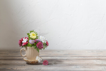 beautiful flowers in cup on wooden table on background white wall