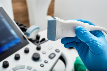 Ultrasound scanner probe in doctor's hand, close-up near ultrasound machine in medical clinic....