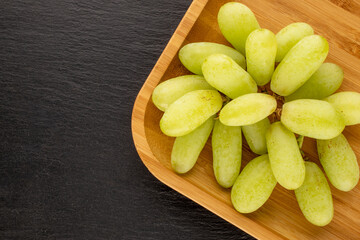 One bunch of white seedless grapes with a bamboo dish on a slate stone, close-up, top view.