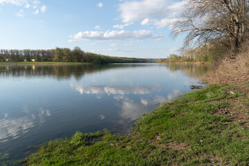 Fototapeta na wymiar Calm scene of Sava river in spring, landscape of river with grassy shore and clouds in sky in spring