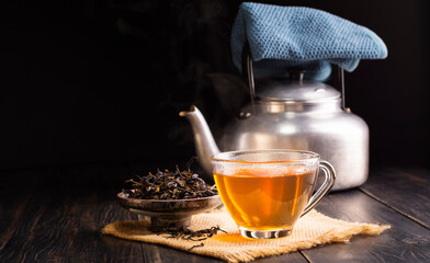 hot herbal teacup and dried tea leaves in a ceramic cup with a tea kettle placed on a black wooden...