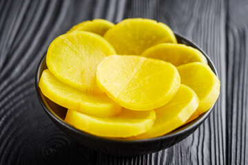 takuan traditional Japanese marinated daikon radish on a dark black rustic wooden background