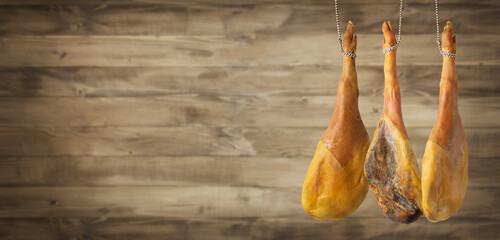 Italian cured ham hanging against wooden background. Copy space