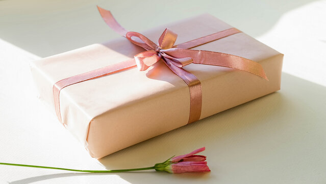 Close up a small gift wrapped with pink ribbon. Gift box on a table with natural light