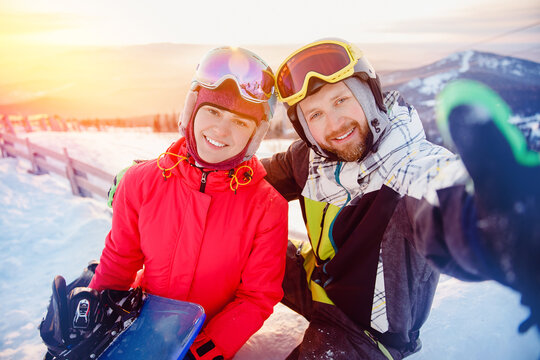 Happy couple snowboarders taking selfie photo with action camera background sunset ski resort. Concept travel love winter