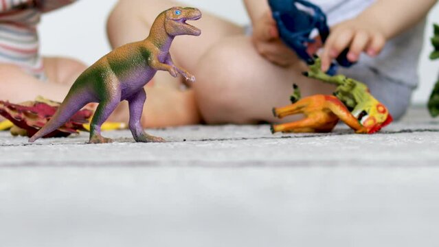 2 brothers,boys, playing with dinosaur toys on grey carpet,in kids room. many species of dino plastic or rubber toys on floor and toddler in background having fun.happy dinosaur day,May 15,june 1