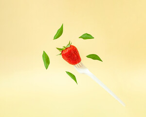 Creative composition with levitating green leaves and red strawberry on a white fork. Healthy food concept.
