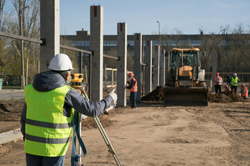 Surveyor engineer with theodolite transit equipment at construction site outdoors during surveying work