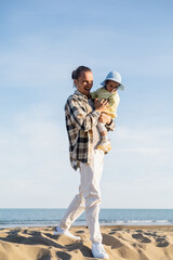 Positive father holding toddler child walking walking on beach in Treviso.