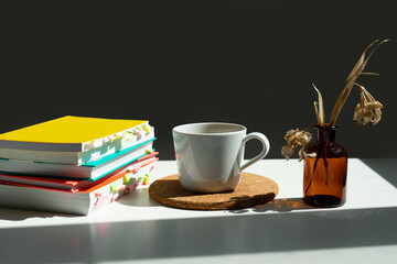 a stack of books on a table with a mug of cha and a vase of dried flowers.