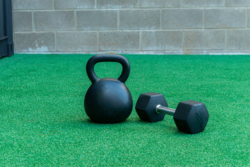 A Kettlebell and a hexagonal dumbbell side by side on synthetic grass