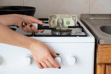One dollar stands on a gas stove and a woman's hand sets fire to a tile in the kitchen at home, the...