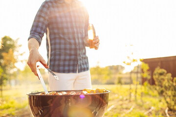 man prepares a barbecue for friends, happy friends make a barbecue outdoors at sunset, A man roasts...