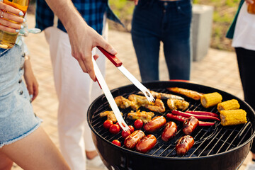 man prepares a barbecue for friends, happy friends make a barbecue outdoors at sunset, man roasts meat on the grill