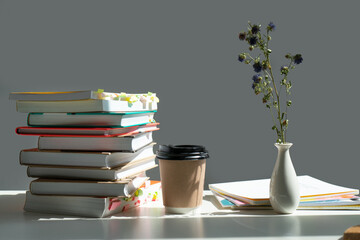 a stack of books on a table with a glass of coffee and a vase of dried flowers.