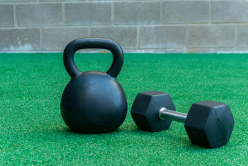 Naklejka na ściany i meble A Kettlebell and a hexagonal dumbbell side by side on synthetic grass