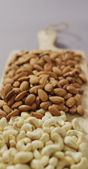 Vertical image of almond and cashew nuts piled on wooden chopping board with lilac background