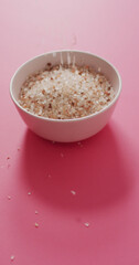 Vertical image of flavoured salt crystals falling into bowl on pink background