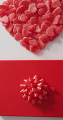 Vertical image of overhead view of red candies in heart shape, and wrapped gift on white