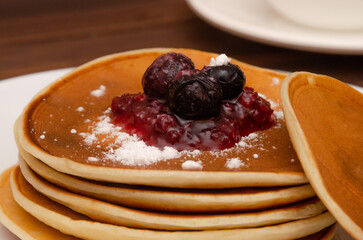 freshly baked pancakes stacked with jam and blueberries on a white plate