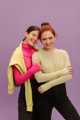 Positive young european girls huddled together posing against purple background. Brunette with eyes closed is holding on to redhead woman. Lifestyle, different emotions, leisure concept. 