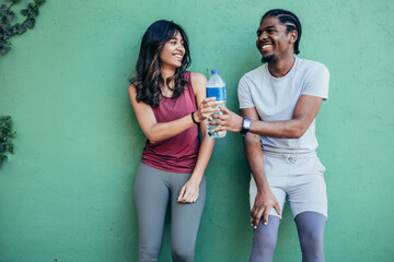 Two athletes resting after hard street workout session leaning on a stone wall. African american...