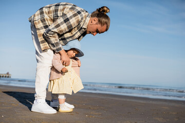 Fototapeta na wymiar Young man wearing jacket on baby girl on beach near adriatic sea in Italy.