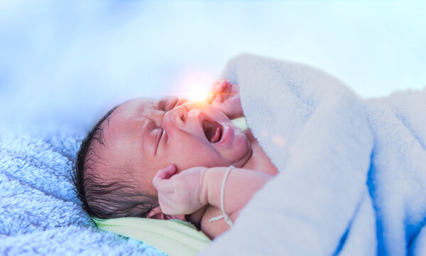 Newborn baby crying new born baby tired and hungry in bed under blue knit blanket. Baby crying baby bedding, baby screaming, healthy baby boy shortly after birth.