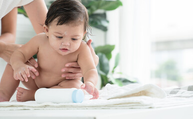Cute Caucasian little naked toddler baby girl sitting on towel after bathing is playing talcum...
