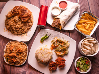Assorted fast food table seekh kabab and tikka biryani, fried rice, fried chicken, seekh kabab shawarma, drink, french fries, raita and salad top view of wooden table
