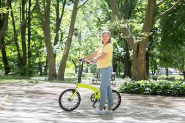 Naklejka premium Retired woman resting in the park, gray-haired Persian woman walks with a bicycle on a summer day