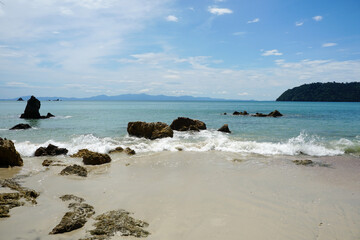 Beautiful and clean sea with waves hitting the sandy beach and quartzite coastal rocks on Koh Phayam Island in Ranong Province, Thailand. 