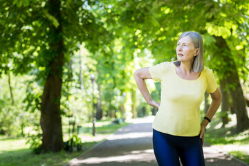 Senior active woman on a walk in the park injured her back, pensioner on a jog on a summer day
