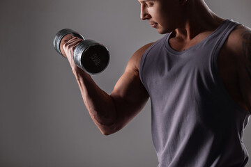 Fototapeta na wymiar Sporty handsome fashionable man with a metal dumbbell working out and pumping muscles on a dark background