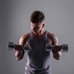 Fototapeta na wymiar Strong powerful sporty man with muscular healthy body with metal dumbbells workout and trains in studio on a gray background