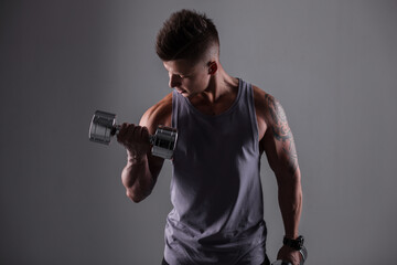 Naklejka na ściany i meble Sporty healthy bodybuilder man with hairstyle and muscular body workout with metal dumbbells on a gray background. Sports lifestyle and fitness